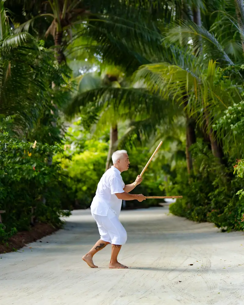 Karol Hasegawa training Filipino Kali martial arts on a palm-lined path in the Maldives