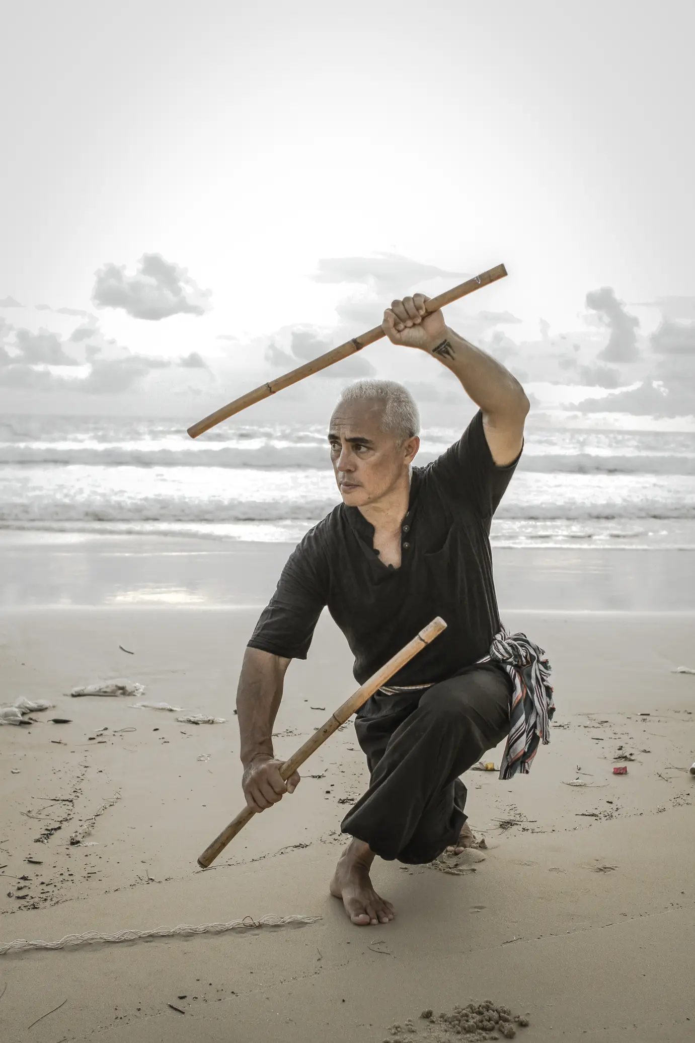Karol Krauser in low Eskrima fighting stance with rattan sticks on Phuket beach