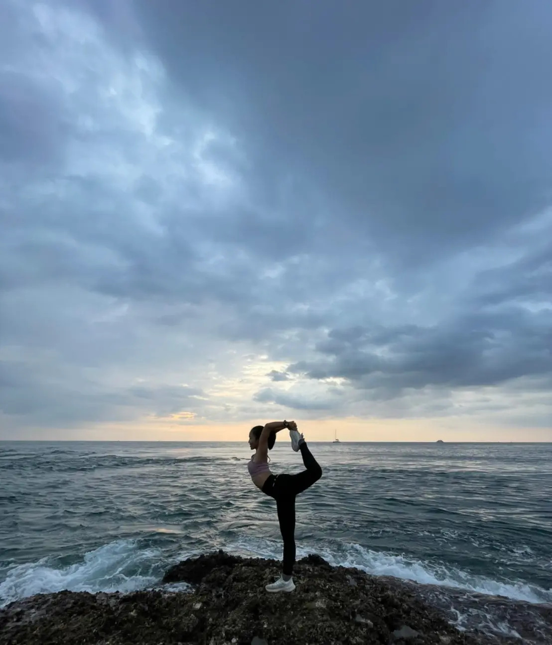 Yoga dancer pose natarajasana on ocean rocks at sunset Phuket Thailand